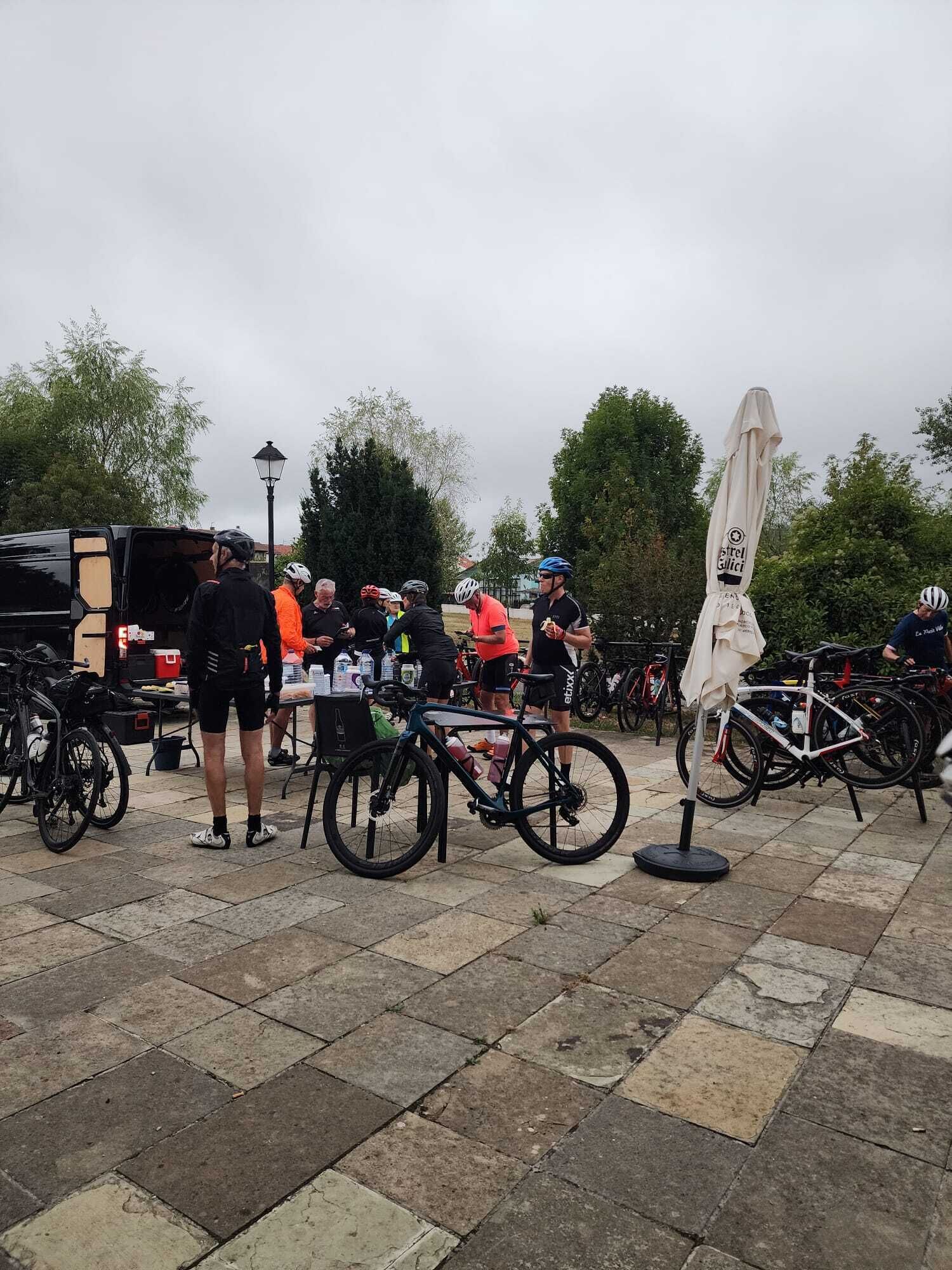 A group of cyclists gathered around a table with refreshments, with bicycles parked nearby.