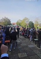 An outdoor gathering with people seated on chairs arranged in rows, facing a central point.