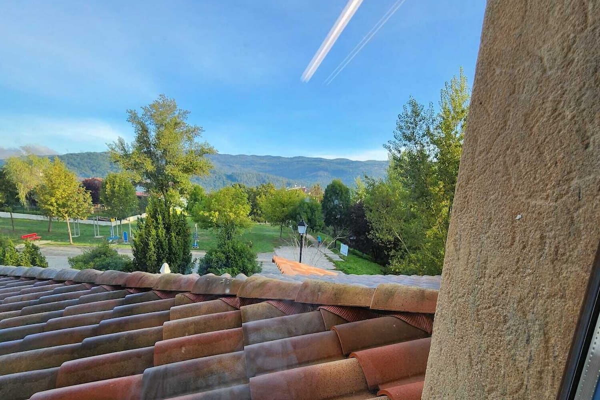 Vista desde una ventana sobre un jardín escalonado, cielo despejado y montañas a lo lejos.
