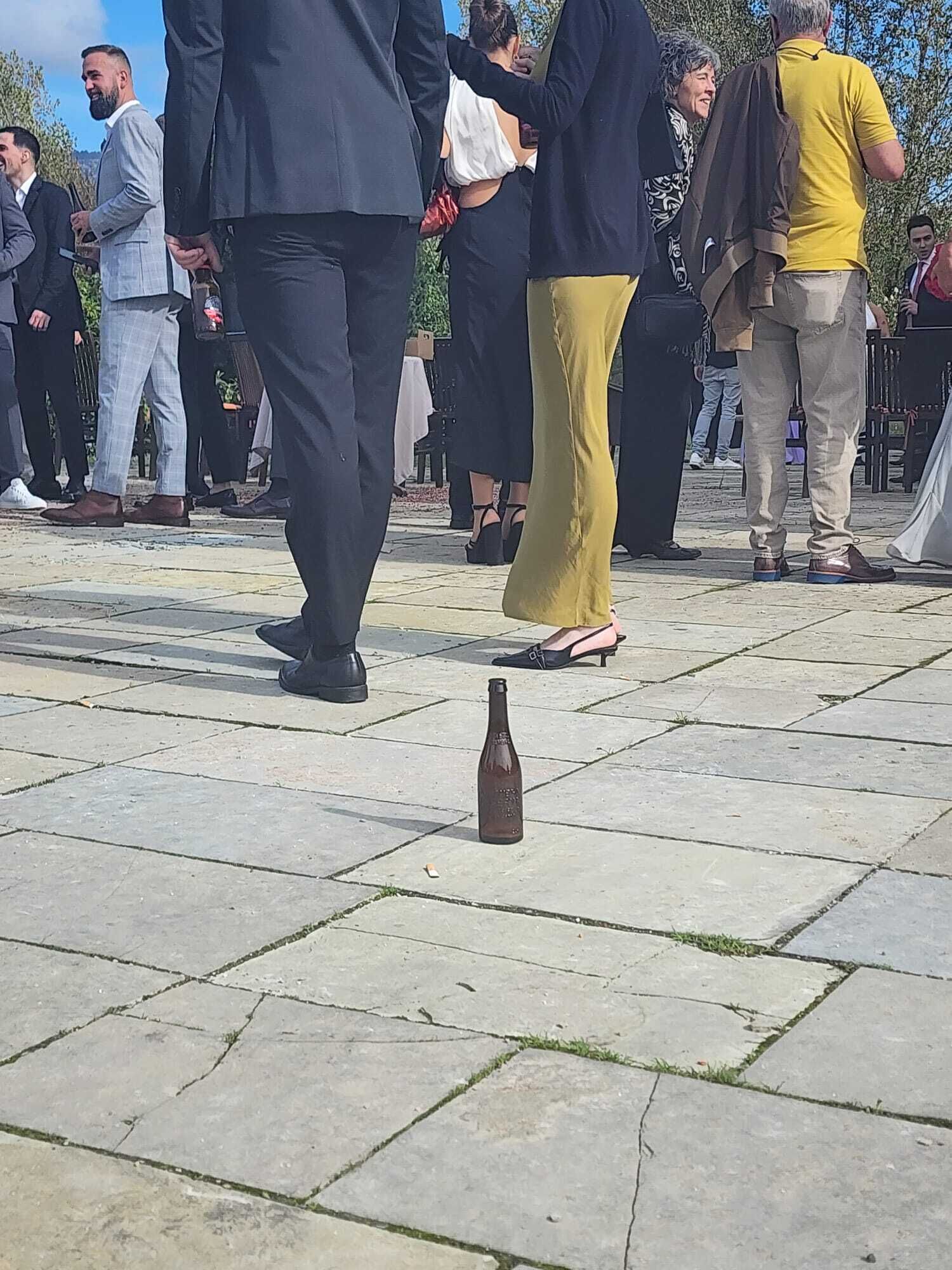 Eine Gruppe von Menschen steht auf einer gepflasterten Fläche im Freien, ein Flaschen liegt auf dem Boden.
