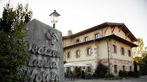 A stone sign with the name "Hotel de la Mare de la Vela" and a building with a tiled courtyard and outdoor seating. - Arbizu (Arbizu)