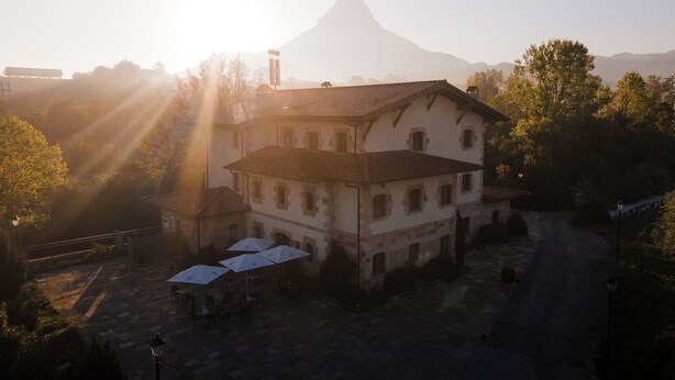 A two-story building with a tiled roof, surrounded by trees and a mountain in the background. - Arbizu (Arbizu)