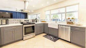 Een moderne keuken met grijze kastjes, roestvrijstalen apparatuur en een groot raam dat voor natuurlijk licht zorgt.