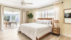 Een slaapkamer met een bed, nachtkastje, plafondventilator, raam met zonwering en uitzicht op de omgeving.