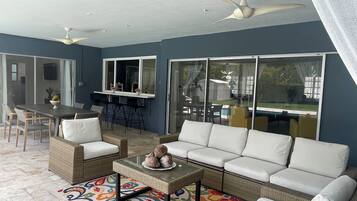 A sunlit patio with a sofa, chairs, a table, and a ceiling fan.