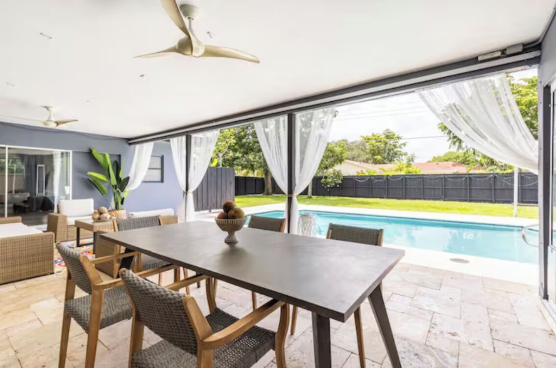 Eine moderne Terrasse mit Esstisch und Stühlen, einem Deckenventilator und Blick auf einen Swimmingpool.