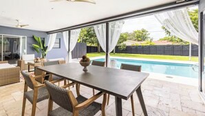 Een modern terras met een eettafel en stoelen, een plafondventilator en uitzicht op een zwembad.