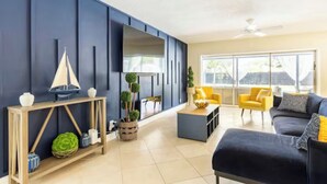 Een moderne woonkamer met een donkerblauwe accentmuur, een houten console en een bank met gele fauteuils.