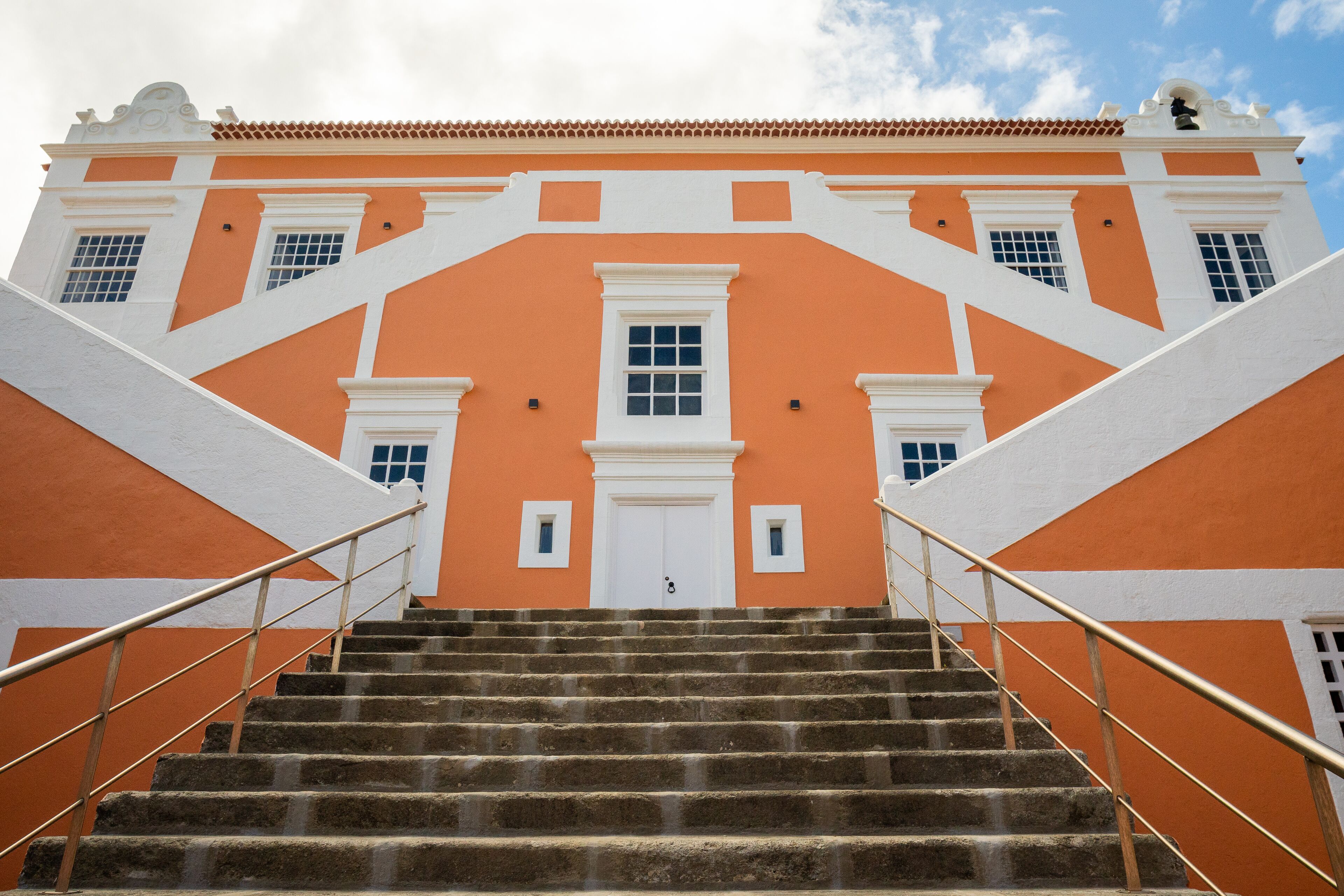 A staircase leading to a building with a white door and windows, surrounded by orange walls and white trim.