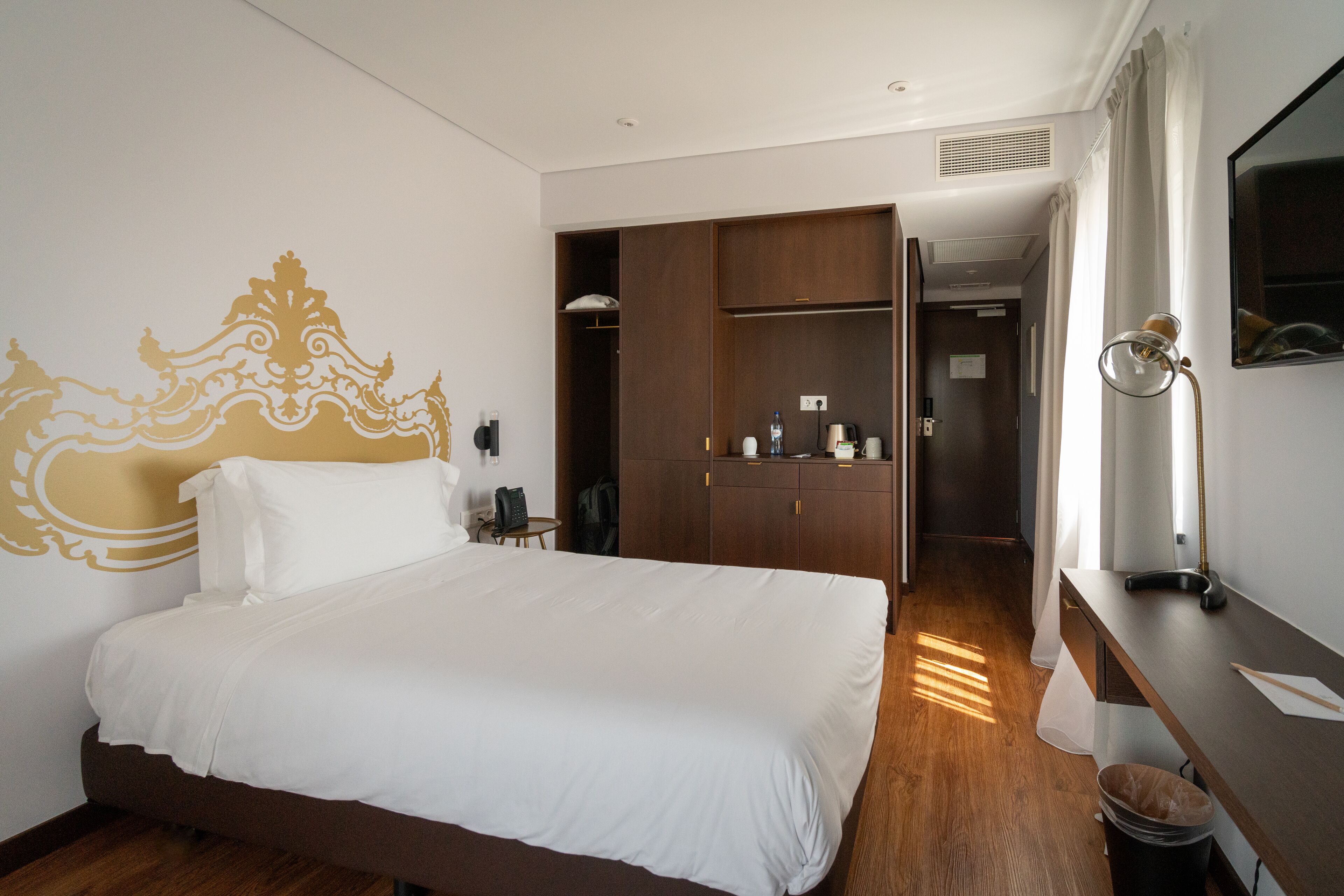 A hotel room with a large bed, a wardrobe, a desk, and a mirror.