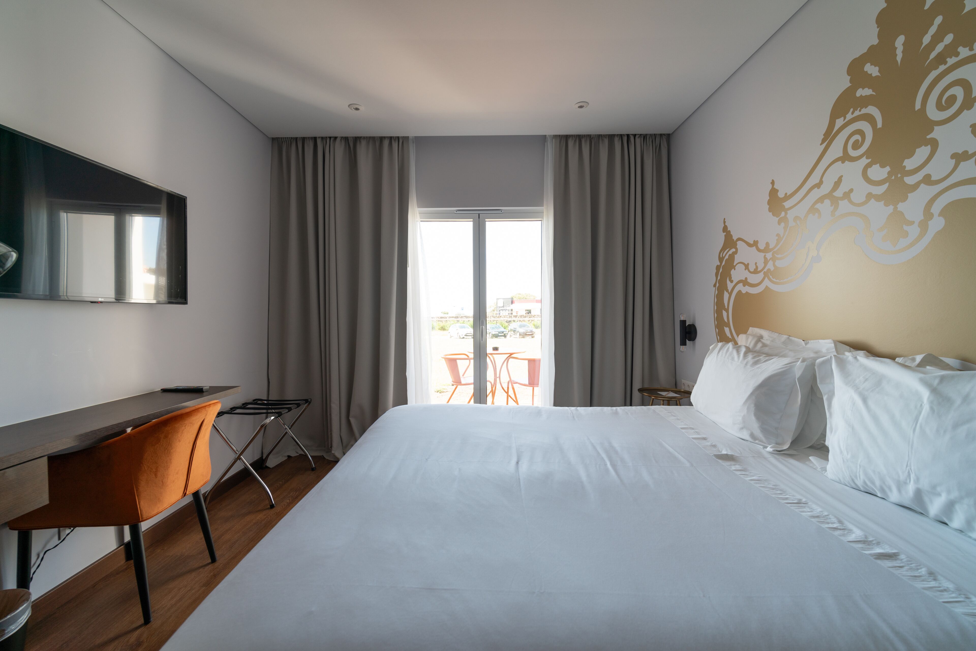 A hotel room with a large bed, a desk, and a view of the outdoors through a sliding door.