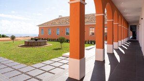 A covered walkway with orange pillars, leading to a building with a tiled roof and a circular fountain in the courtyard. - Palacio Santa Catarina Hotel (Angra do Heroismo)
