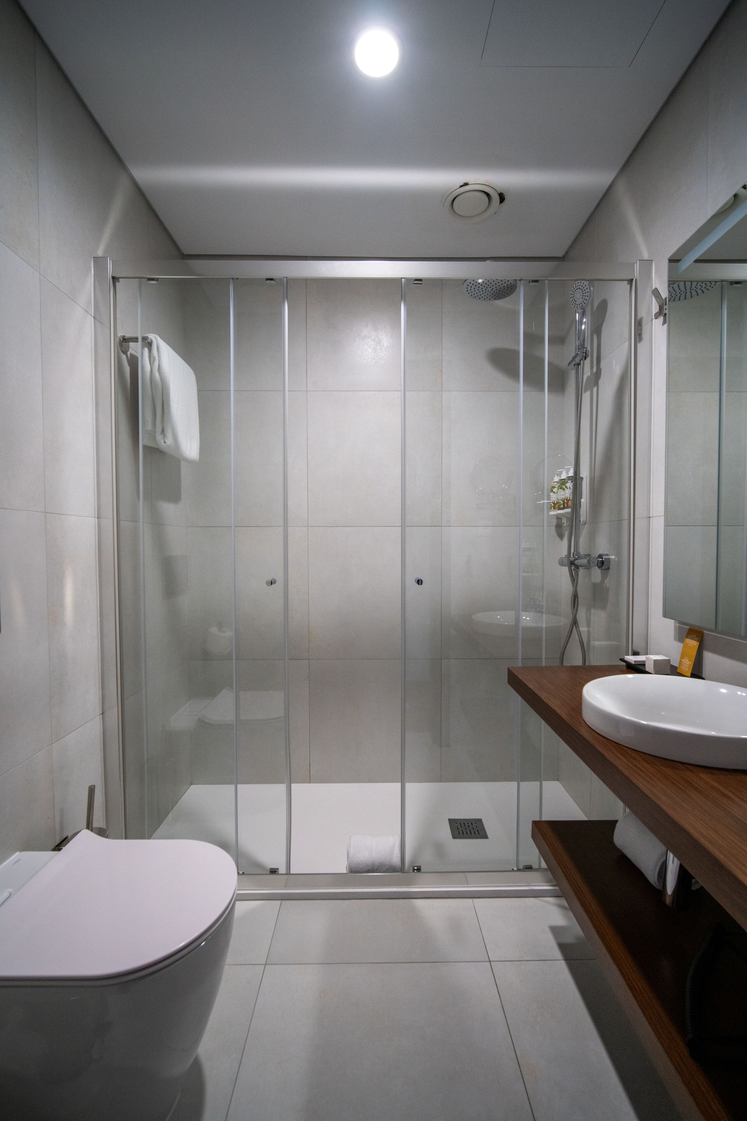 Une salle de bain moderne avec une douche à parois de verre, des toilettes blanches et un meuble-lavabo en bois avec un évier.