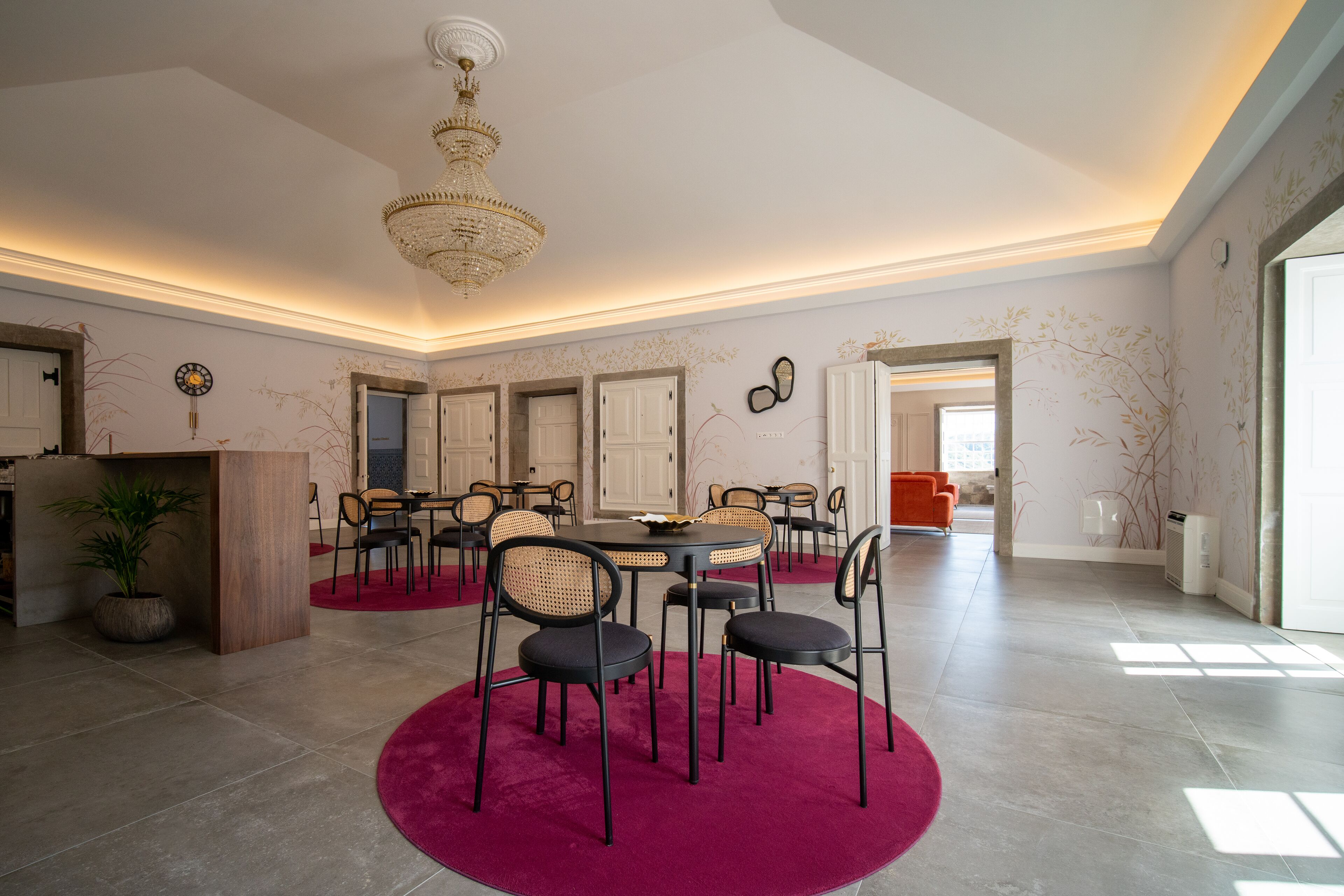 Uma sala de jantar ampla com um lustre, mesas redondas e cadeiras.