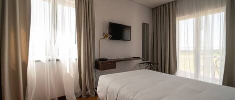 A modern hotel room with a large bed, a mounted TV, and a balcony view.