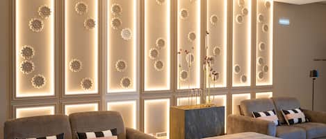 A modern living room with two sofas, a coffee table, and a decorative wall with illuminated floral patterns.