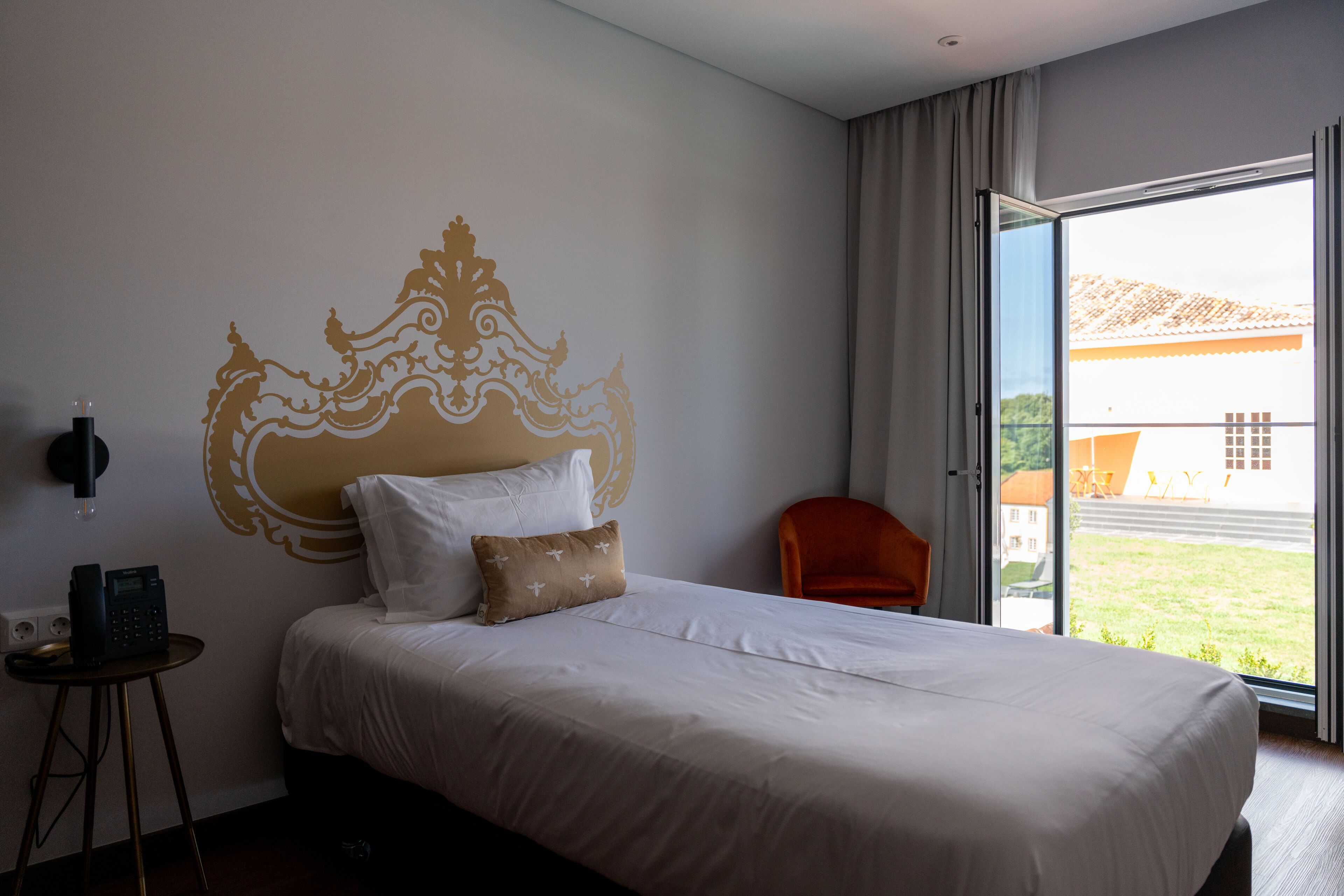 A hotel room with a large bed, a small table with a phone, and a view through a sliding glass door.