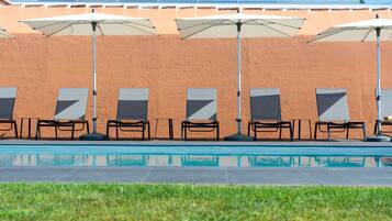 A poolside area with lounge chairs and umbrellas, a clear pool, and a brick wall in the background.