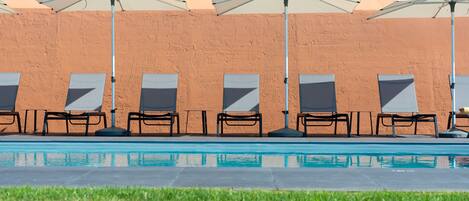 A poolside area with lounge chairs and umbrellas, a clear pool, and a brick wall in the background.