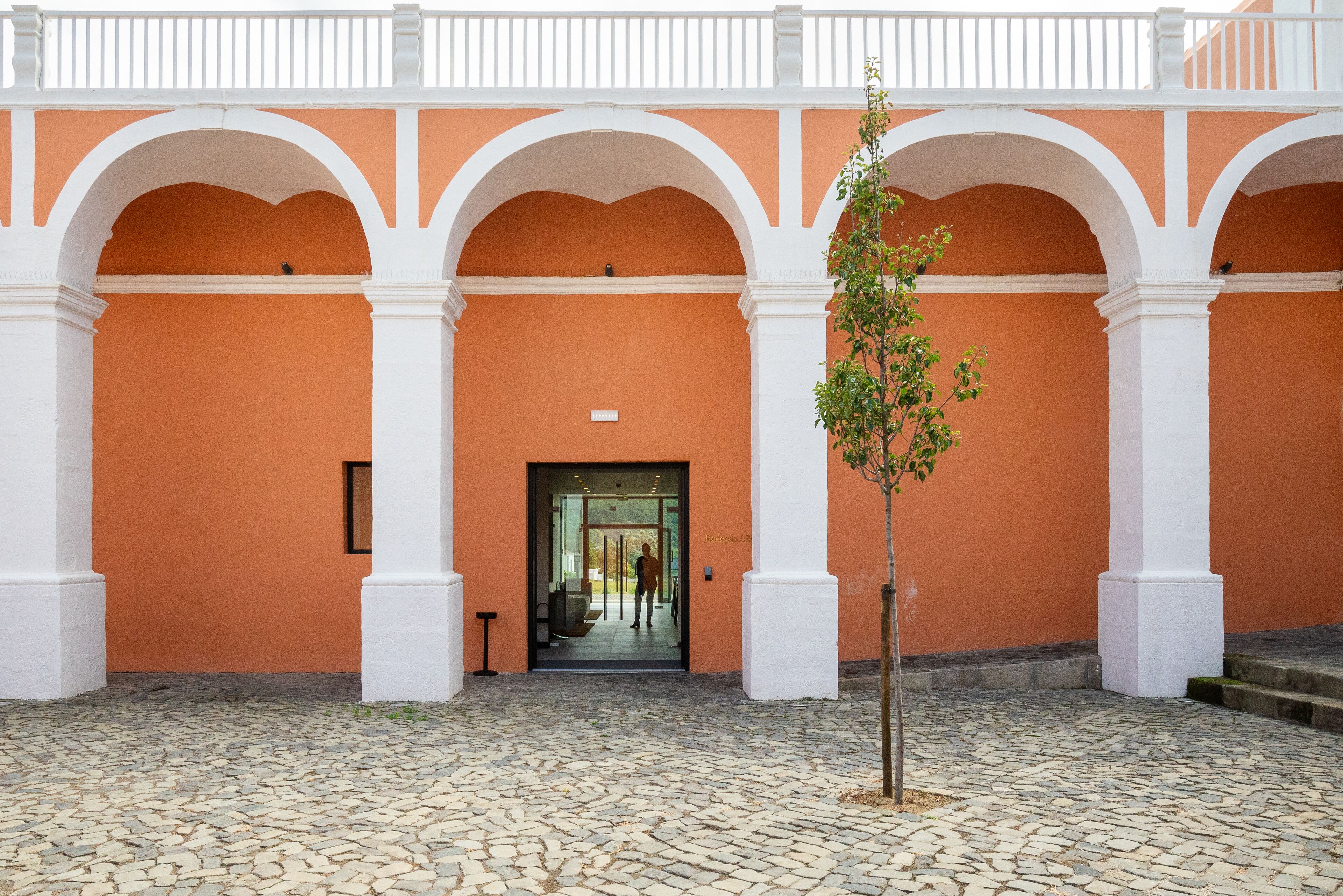 Un patio con piso de adoquines, arcos blancos y una pared anaranjada.