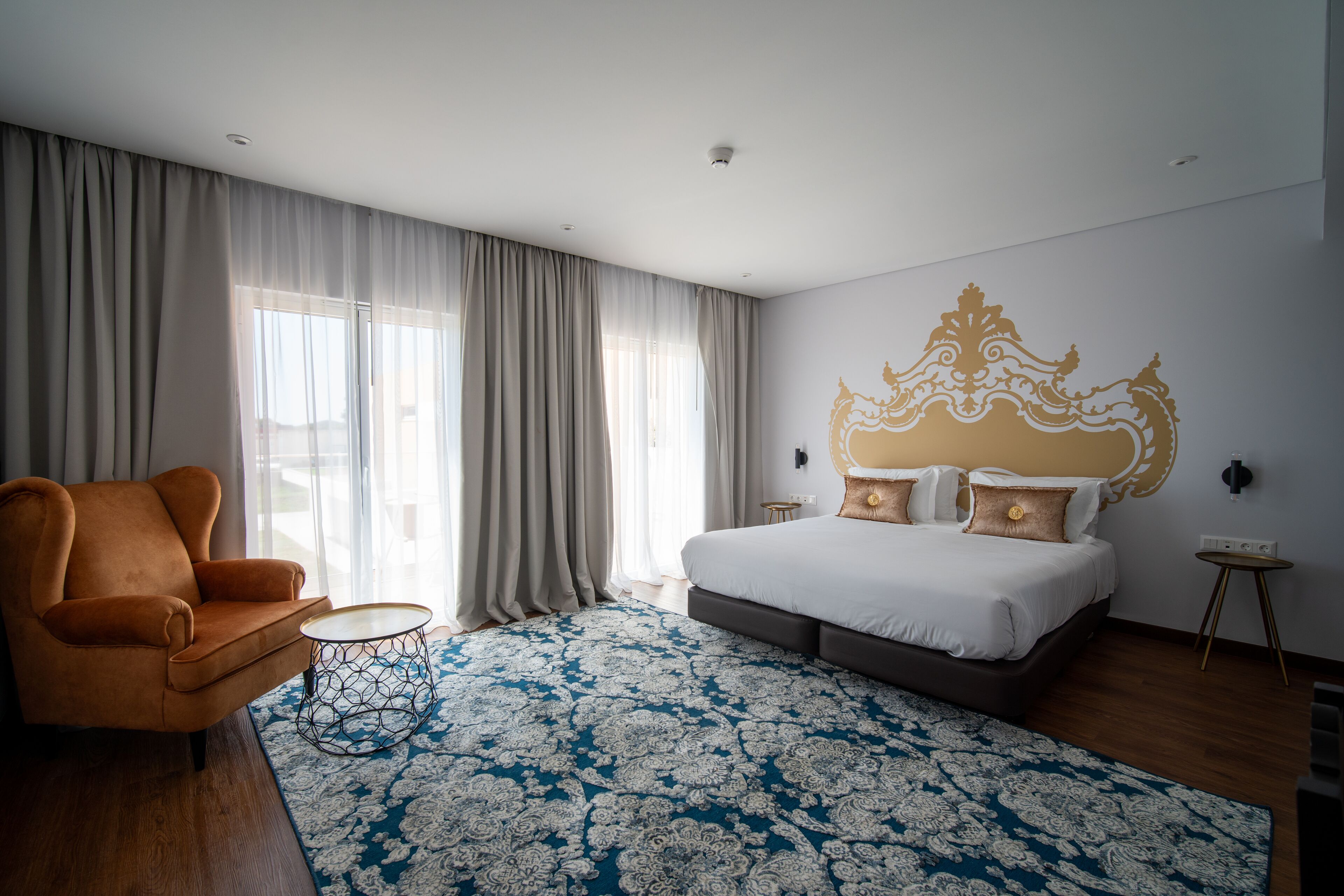 A modern hotel room with a large bed, a sofa, a small round table, and a decorative wall piece.
