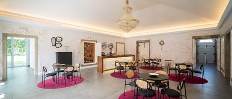 Une pièce spacieuse agrémentée d’un lustre, d’un comptoir d’accueil et de plusieurs espaces aménagés avec des tables et des chaises rondes.