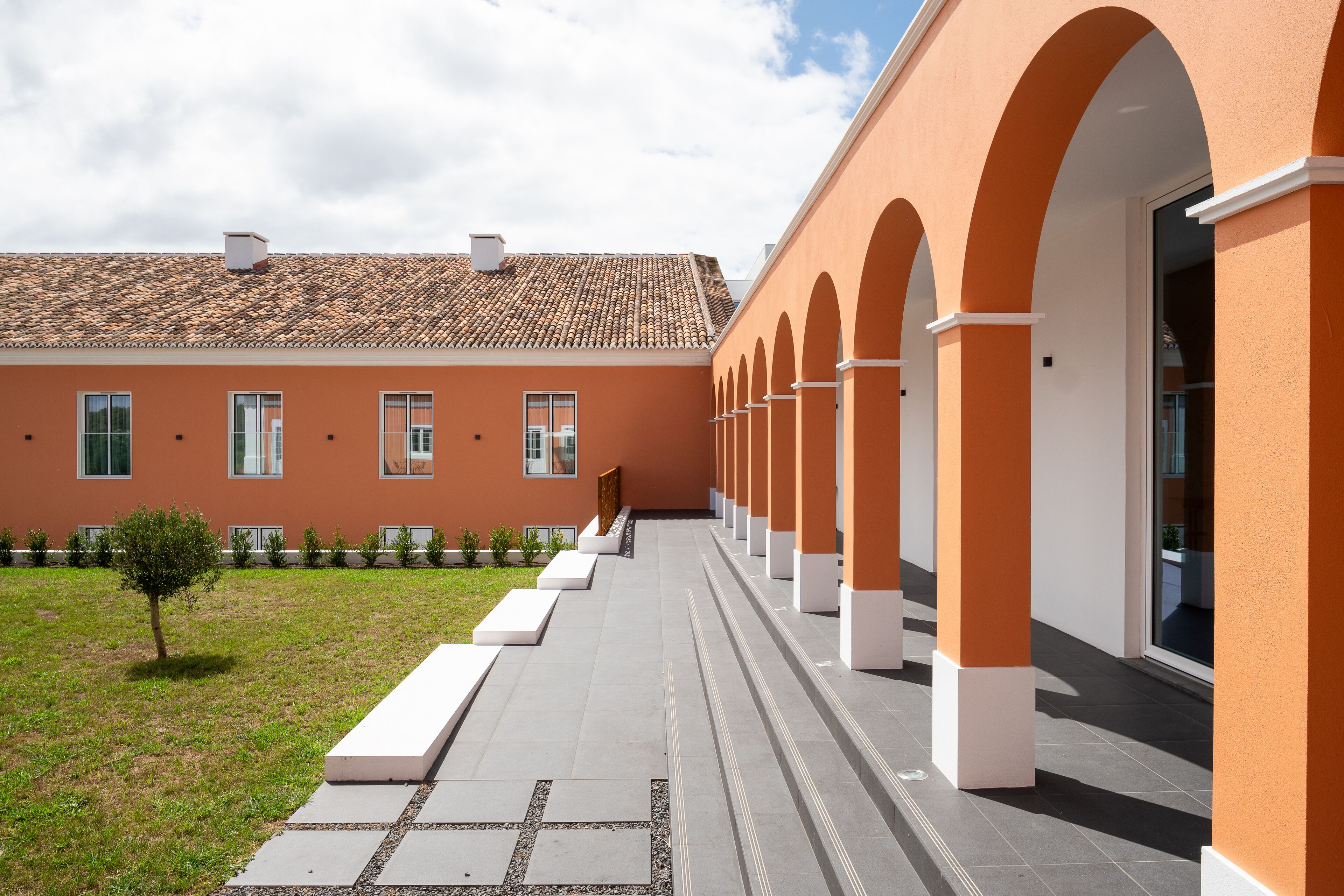 A building with a tiled roof, a courtyard with a pathway, and a row of arches.