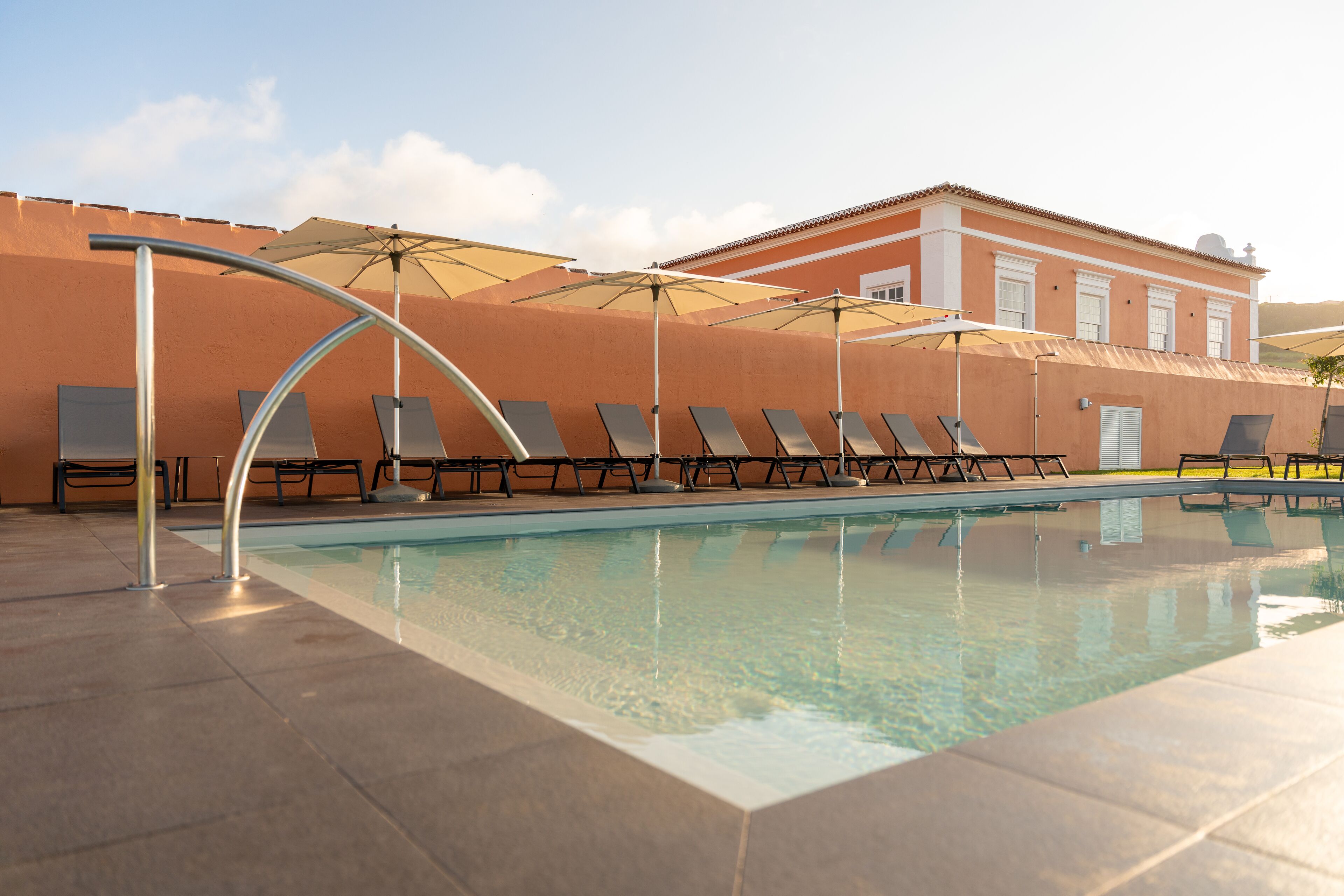 Una piscina con tumbonas y sombrillas, rodeada de un patio con baldosas.