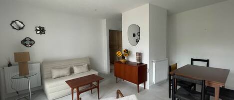 A modern living room with a sofa, coffee table, dining table, and chairs. There is a radiator, a lamp, and wall decorations.