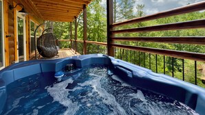 Een hottub op een houten terras met uitzicht op bomen en een heldere lucht.