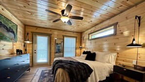 Een slaapkamer in een houten chalet, met een bed, een kaptafel, een plafondventilator en een groot raam.