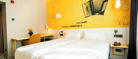 A hotel room with a large bed, a desk, a chair, and a wall with musical instruments and the text "sleep well our music is relaxing".