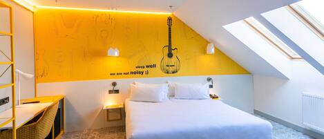 A bedroom with a bed, a desk, a chair, a wall with a guitar illustration, and skylights.
