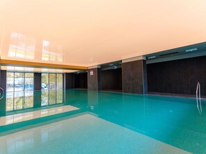 An indoor swimming pool with clear glass walls, a tiled floor, and a dark wall on one side.
