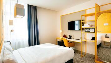 Ein Hotelzimmer mit Bett, Schreibtisch mit Stuhl, Fernseher und Spiegel.