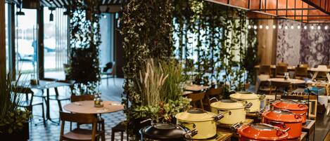 Un interior de restaurante con mesas, sillas y plantas colgantes.