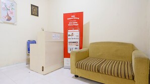 A room with a beige sofa, a small table, and a refrigerator. There is a poster on the wall and a blue chair. - Hotel O Wisma Pinggir (Tanjung Pinang)