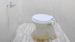 A small, white-tiled bathroom with a toilet, a shower area, and a wall-mounted faucet. - Hotel O Wisma Pinggir (Tanjung Pinang)