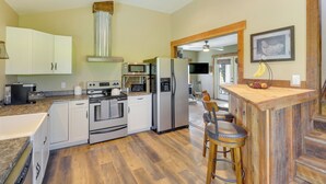 Een moderne keuken met witte kasten, roestvrijstalen apparatuur, een bartable en uitzicht op de eetruimte.