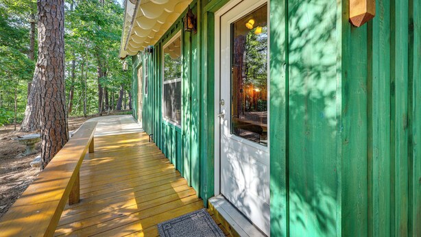A wooden deck leading to a green building with a door and windows, surrounded by trees. - Pet-Friendly Eureka Springs Rental w/ Private Deck (Eureka Springs)