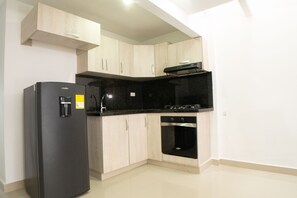 Een koelkast, een oven, een kookplaat, kookgerei, borden en bestek