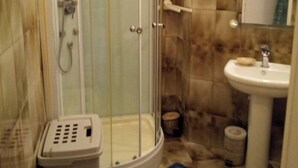 A shower with a glass door, a white sink, and a small trash bin.