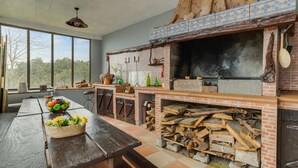 Una cocina rústica con horno de ladrillo, mesa de madera y un ventanal con vistas a árboles.