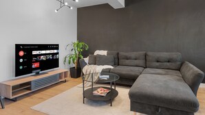 Una sala de estar moderna con un sofá modular, una mesa de centro de vidrio, un televisor de pantalla plana y una planta en maceta.