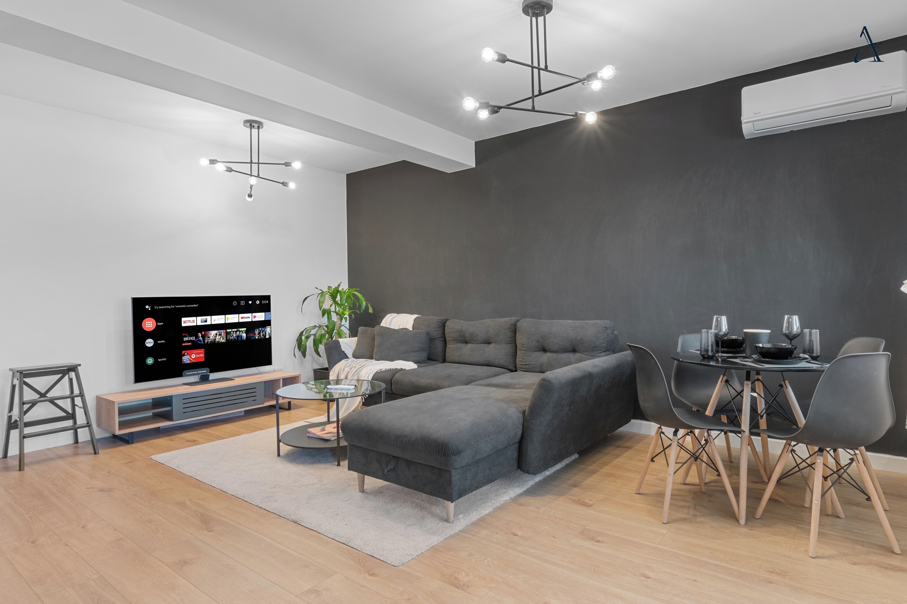 Een moderne woonkamer met een hoekbank, een eettafel met stoelen, een flatscreen televisie en een potplant.
