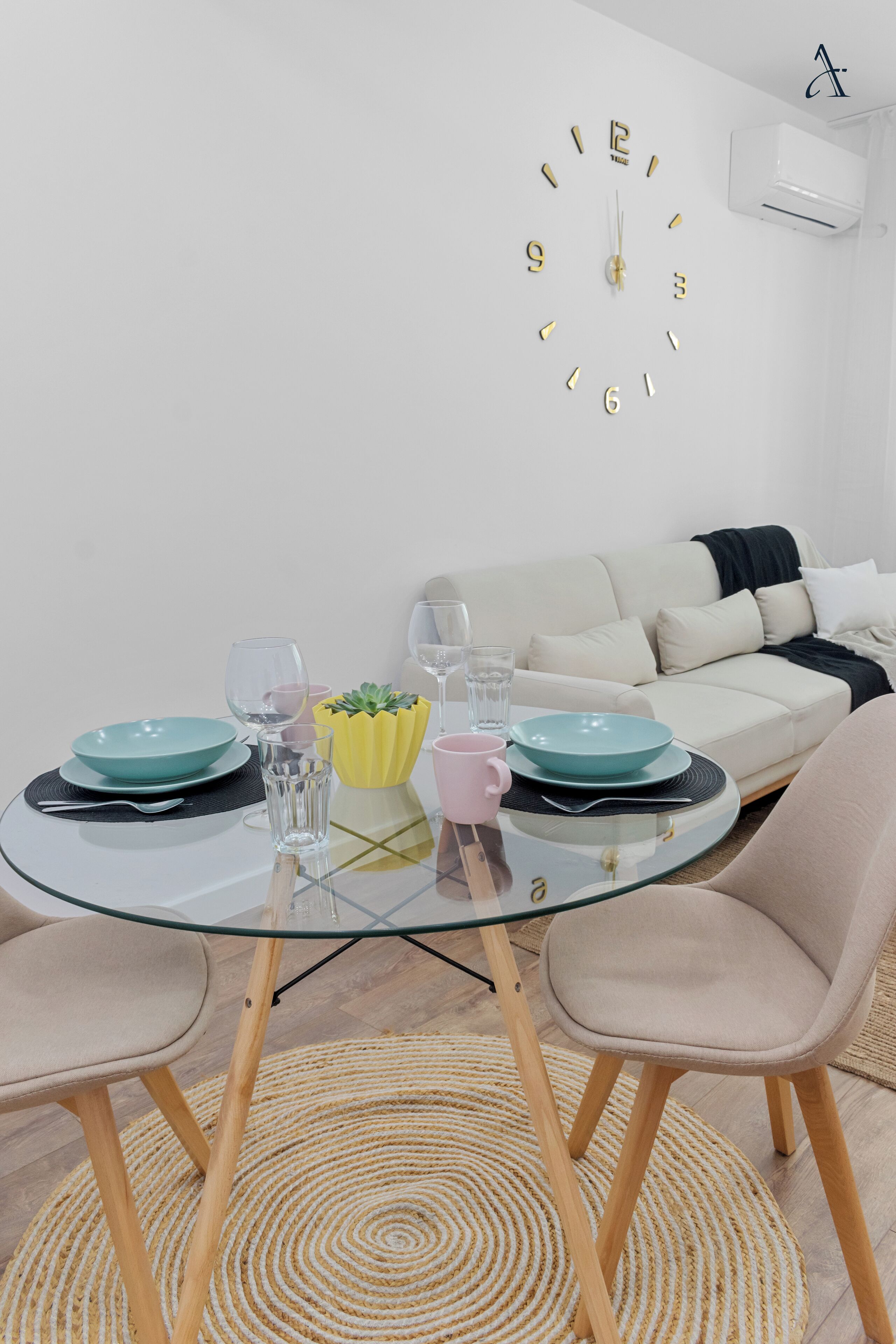 A modern living room with a round glass table, two chairs, a sofa, and a wall clock.