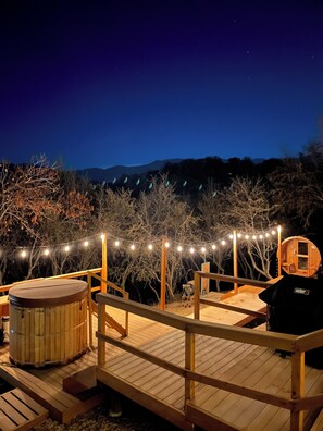 A wooden deck with a hot tub, wooden chairs, and a wooden structure with a window.