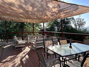 Ein überdachter Außenbereich mit Holzdeck, gepolsterten Stühlen und einem Glastisch.