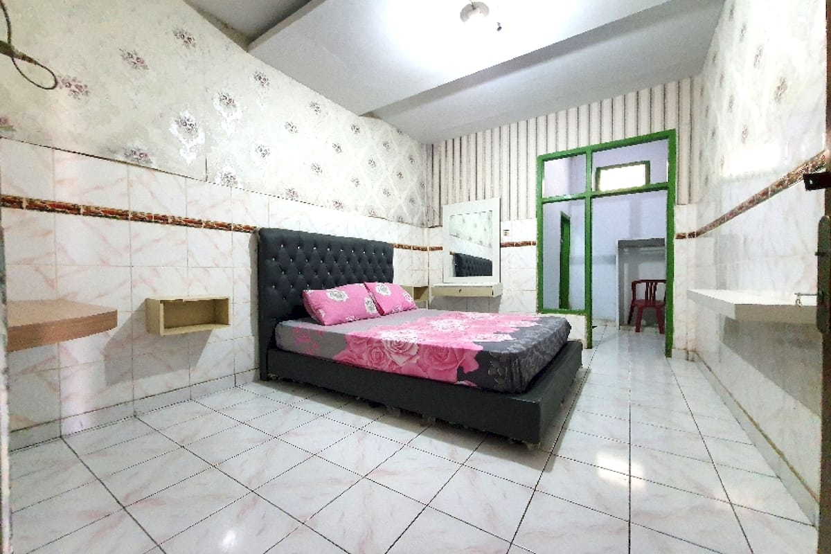 Une chambre à coucher avec un lit, une table de chevet, un miroir et une porte dont le cadre est vert.