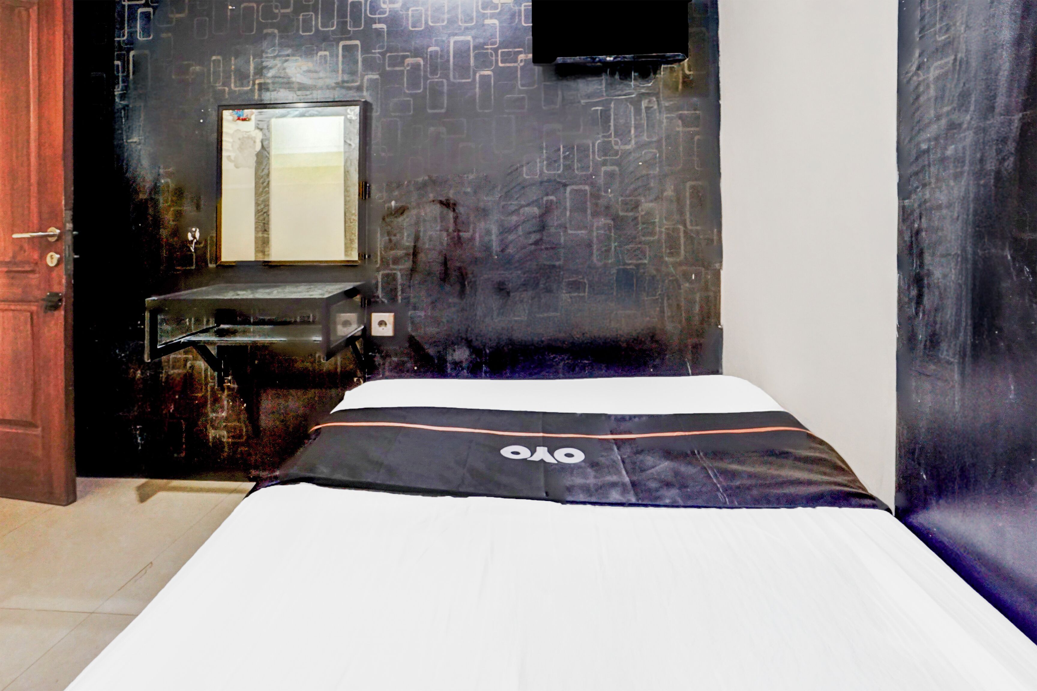 Una habitación de hotel con una cama, un escritorio pequeño, un espejo y un televisor montado en la pared.